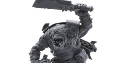 AdeptiCon 2026 promo miniatures featuring an Ork and Space Marine from Warhammer 40,000, showcased in a tabletop wargaming review.